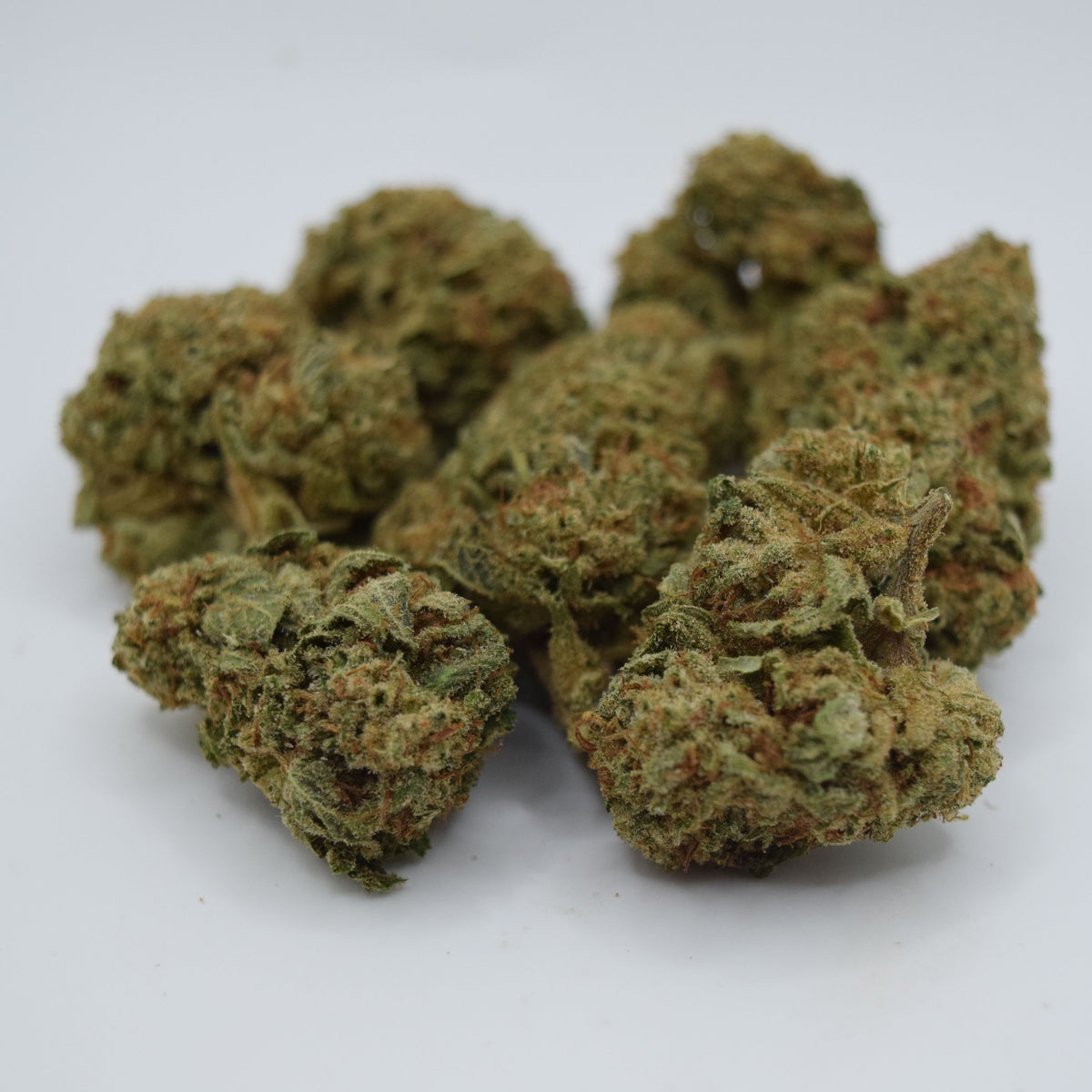 A pile of dried cannabis buds with green and orange-brown tones, photographed on a plain white background.
