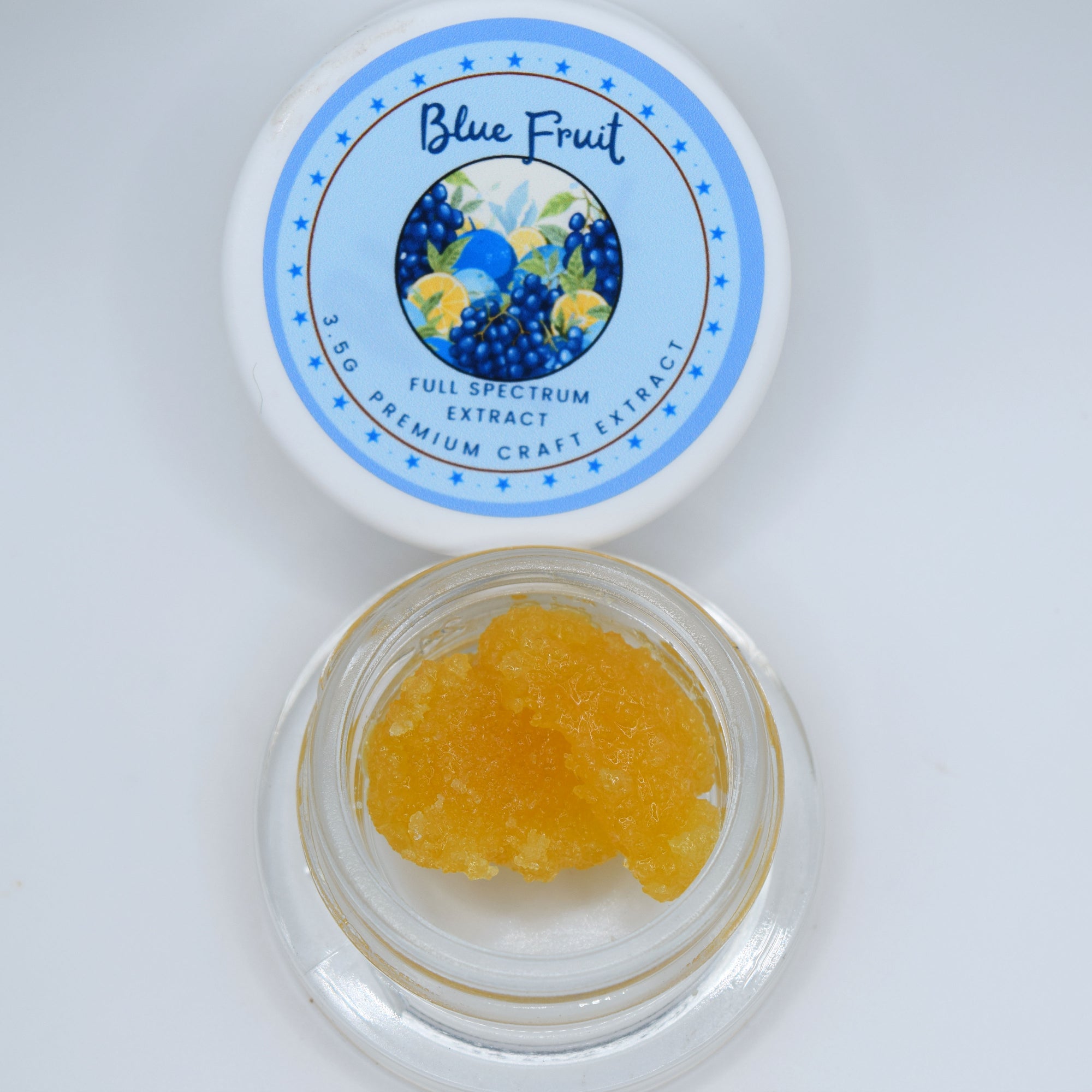 An open clear jar filled with yellow-orange crystalline powder sits below its white lid, which features a blue circular label reading 'Blue Fruit Full Spectrum Extract'.
