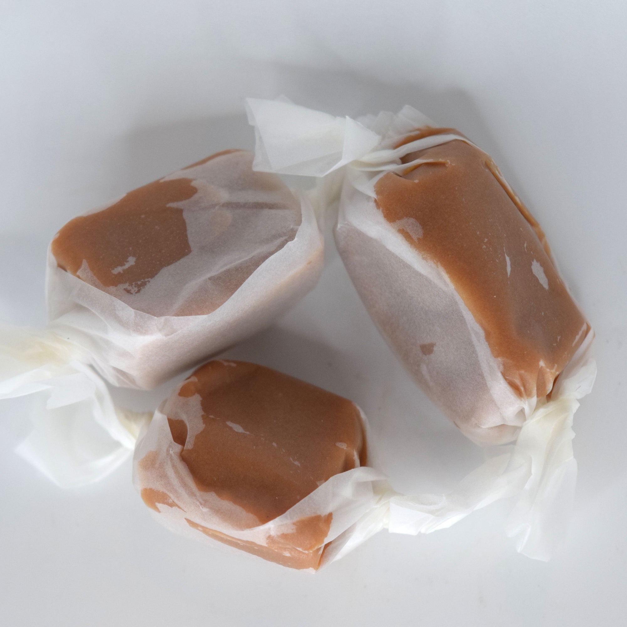 Three wrapped caramel candies with white tissue paper wrappers, arranged on a plain white background.