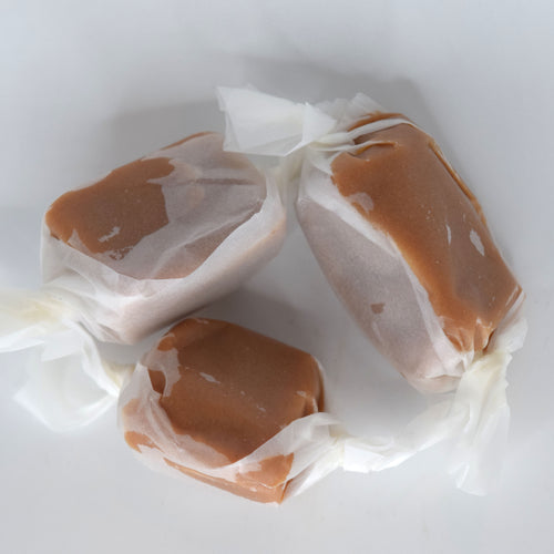 Three wrapped caramel candies with white tissue paper wrappers, arranged on a plain white background.
