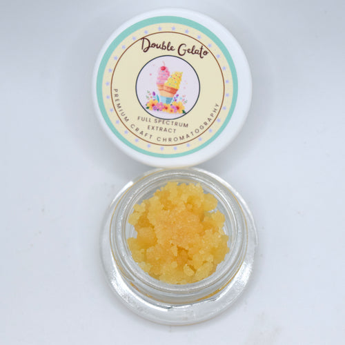 A small clear round jar filled with yellow-orange gel crystals sits below its white lid, which has a colorful label reading 'Double Gelato' and 'Full Spectrum Extract'.
