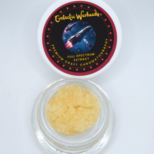 A small clear jar filled with pale yellow crystalline powder sits below its white lid, which features a circular black and red label reading Galactic Warheads Full Spectrum Extract.