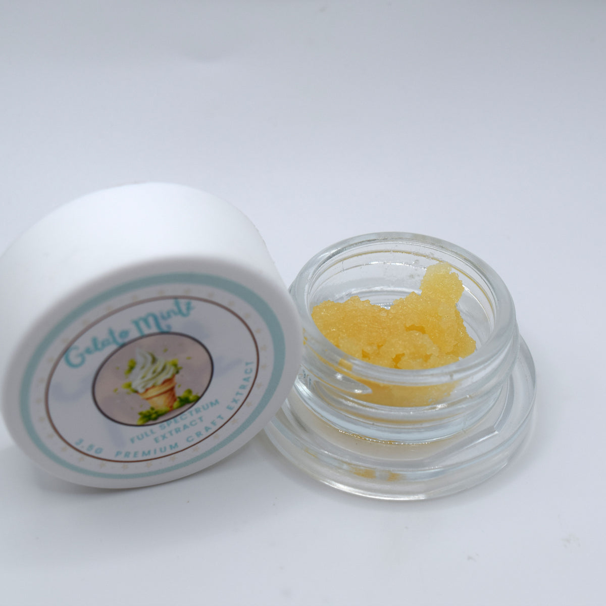 A small clear glass jar containing yellow gel scrub, shown next to its white lid which features a circular label reading 'Gelato Mints'.