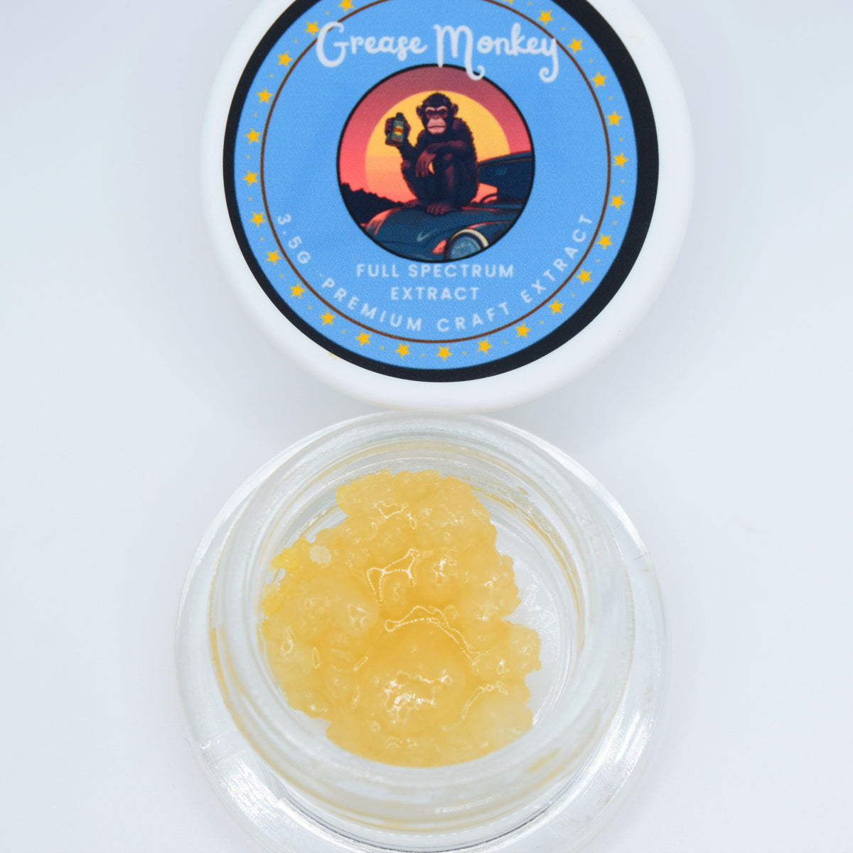 An open clear jar showing a yellow translucent gel-like product, with the white lid above it printed with the brand name Grease Monkey and 'Full Spectrum Extract'.