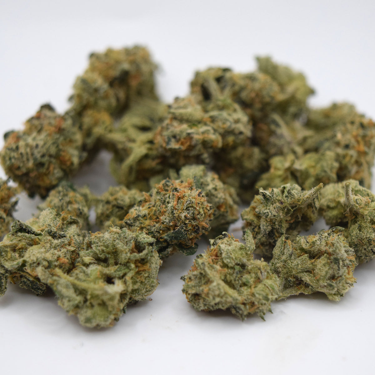 A pile of dried cannabis buds with green and orange coloration, photographed on a plain white background.