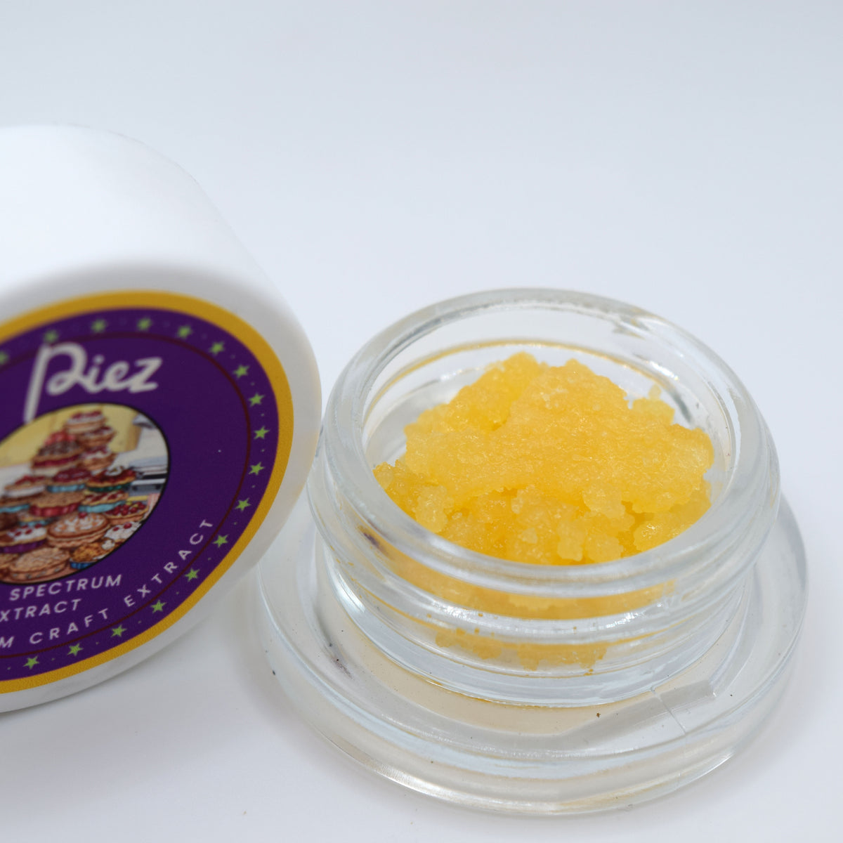 A small clear glass jar filled with bright yellow crystalline powder sits beside its white lid, which features a purple and gold label reading 'Piez Spectrum Extract Craft Extract'.