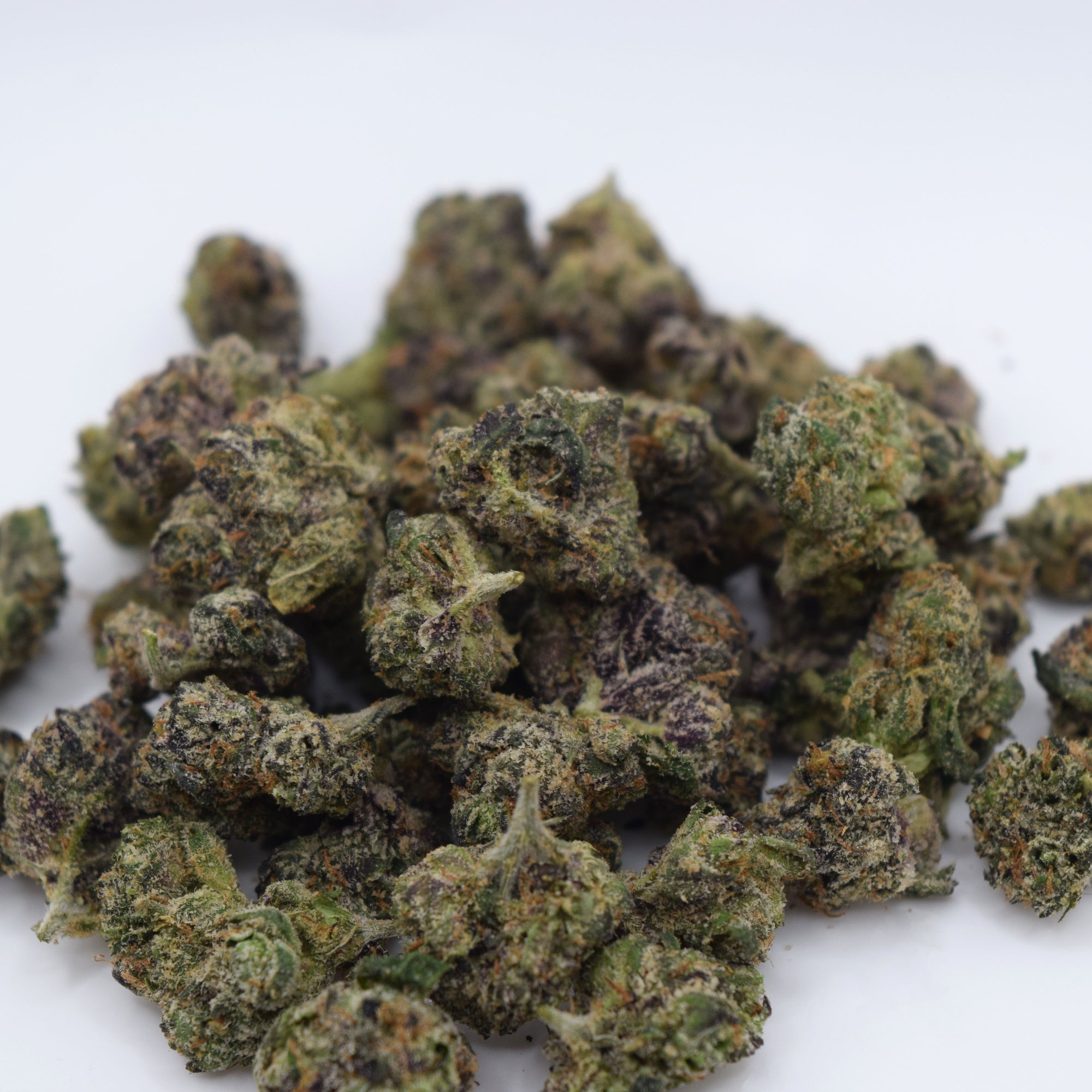 A pile of dried cannabis buds with green, orange, and purple hues, photographed on a plain white background.