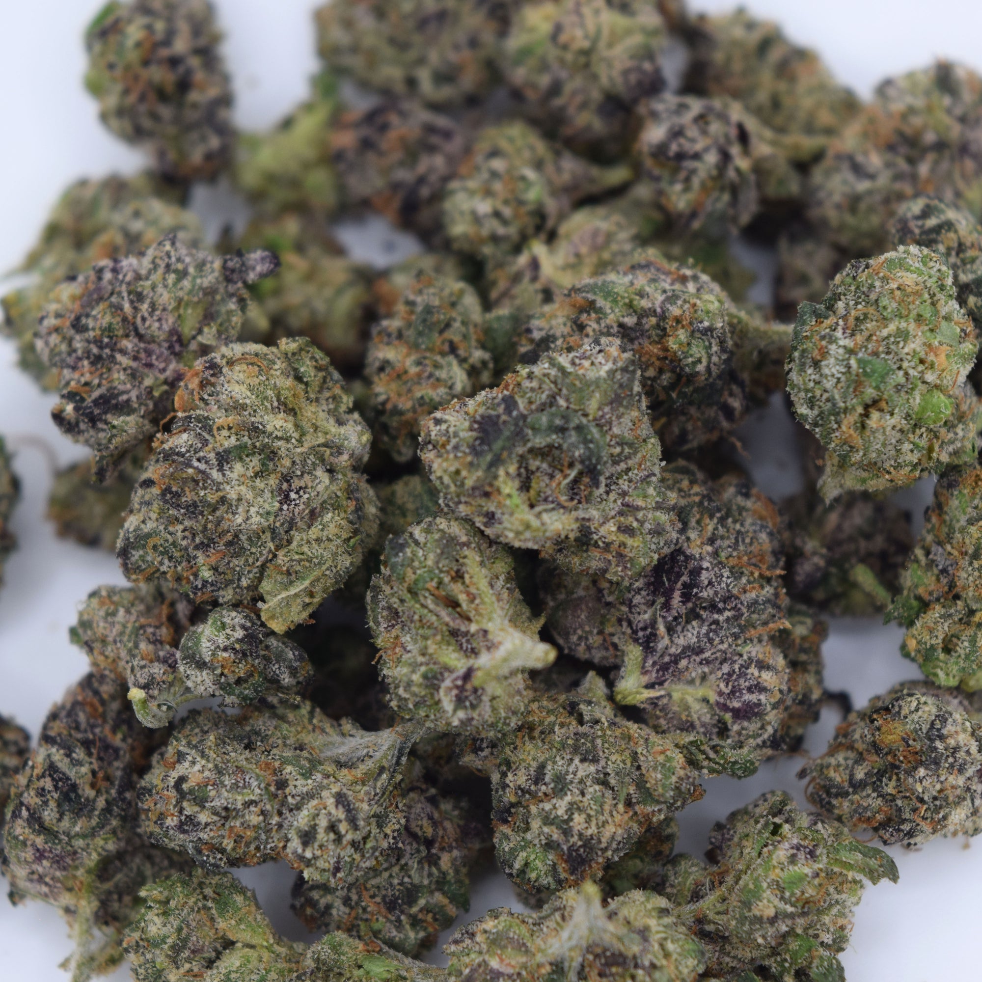 A close-up pile of dried cannabis buds with green, purple, and orange tones on a white background.