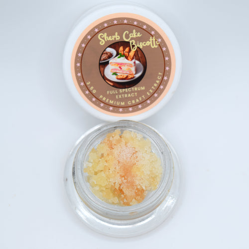 An open round glass jar containing pale yellow crystalline powder, with its white lid placed above. The lid features a brown circular label reading 'Sherb Cake Biscotti' and 'Full Spectrum Craft Extract'.