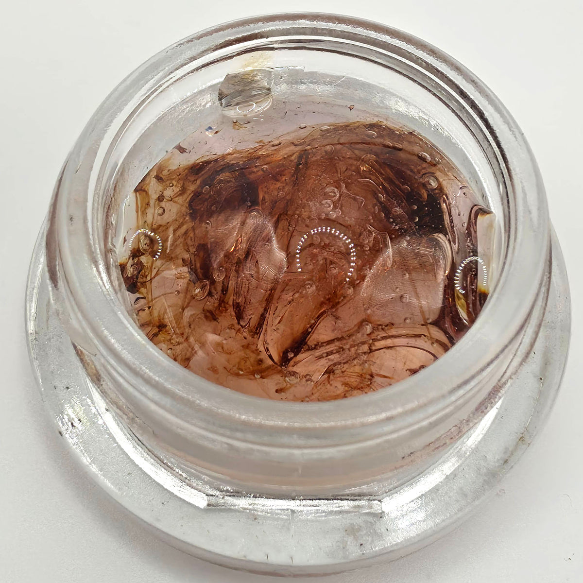 A clear glass jar containing a brown translucent liquid or wax with embedded circular dotted details, photographed from above on a white background. Pure THCV tetrahydrocannabivarin cannabinoid isolate for functional cannabinoid formulations, tinctures, capsules, edibles, and custom blends.