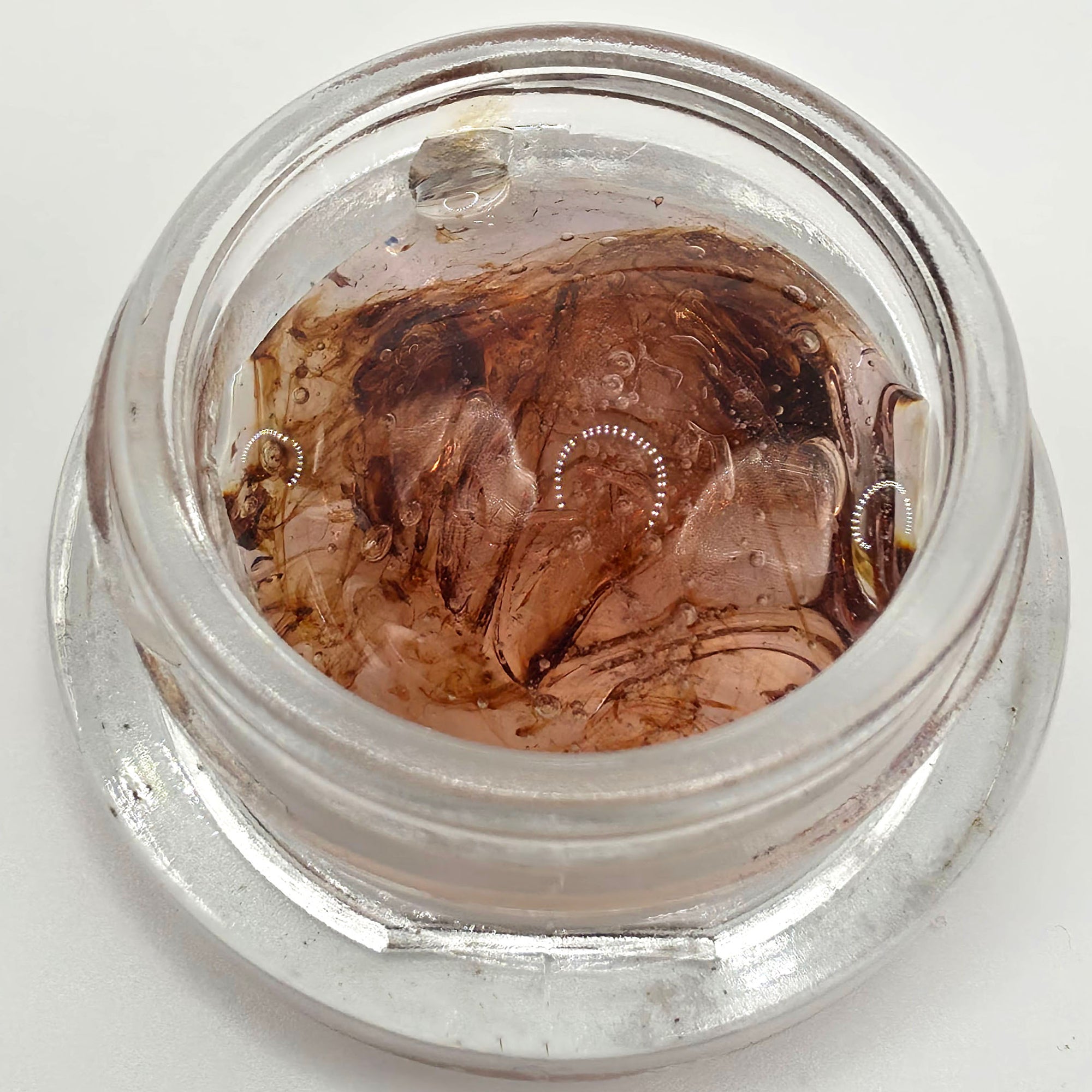 A clear glass jar containing a brown translucent liquid or wax with embedded circular dotted details, photographed from above on a white background. Pure THCV tetrahydrocannabivarin cannabinoid isolate for functional cannabinoid formulations, tinctures, capsules, edibles, and custom blends.